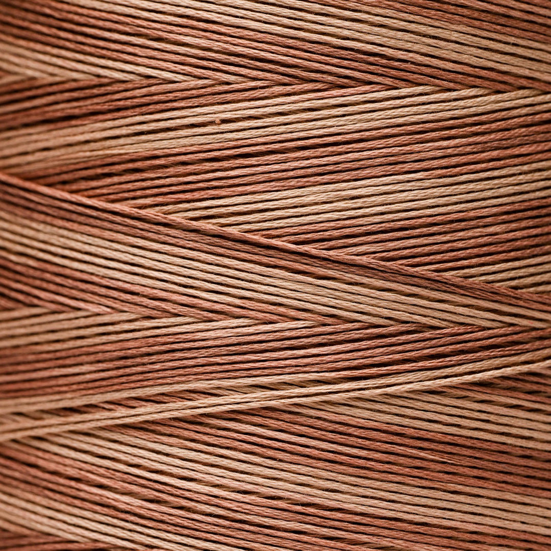 A close-up texture shot of thread in a warm copper-brown and tan colorway, wrapped as though around a spool 