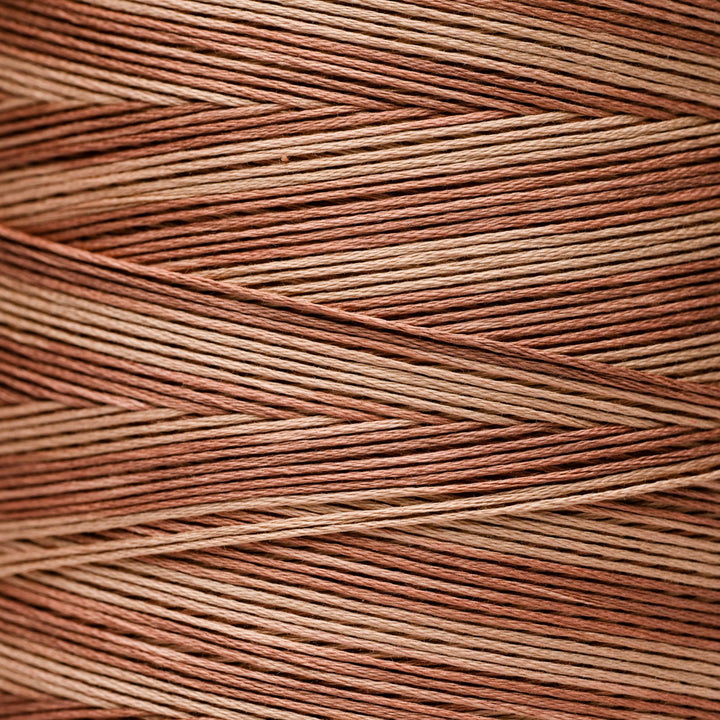 A close-up texture shot of thread in a warm copper-brown and tan colorway, wrapped as though around a spool 