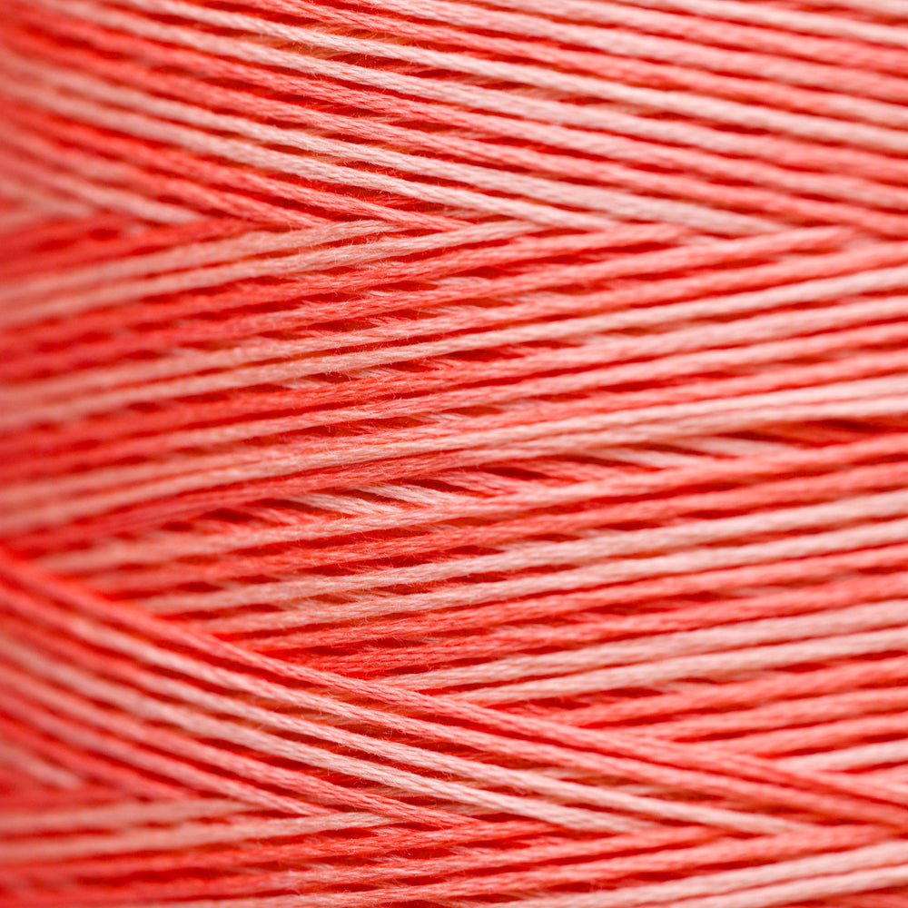 A close-up of tightly wound yarn or thread in a coral-red and pale pink colorway, filling the entire frame.