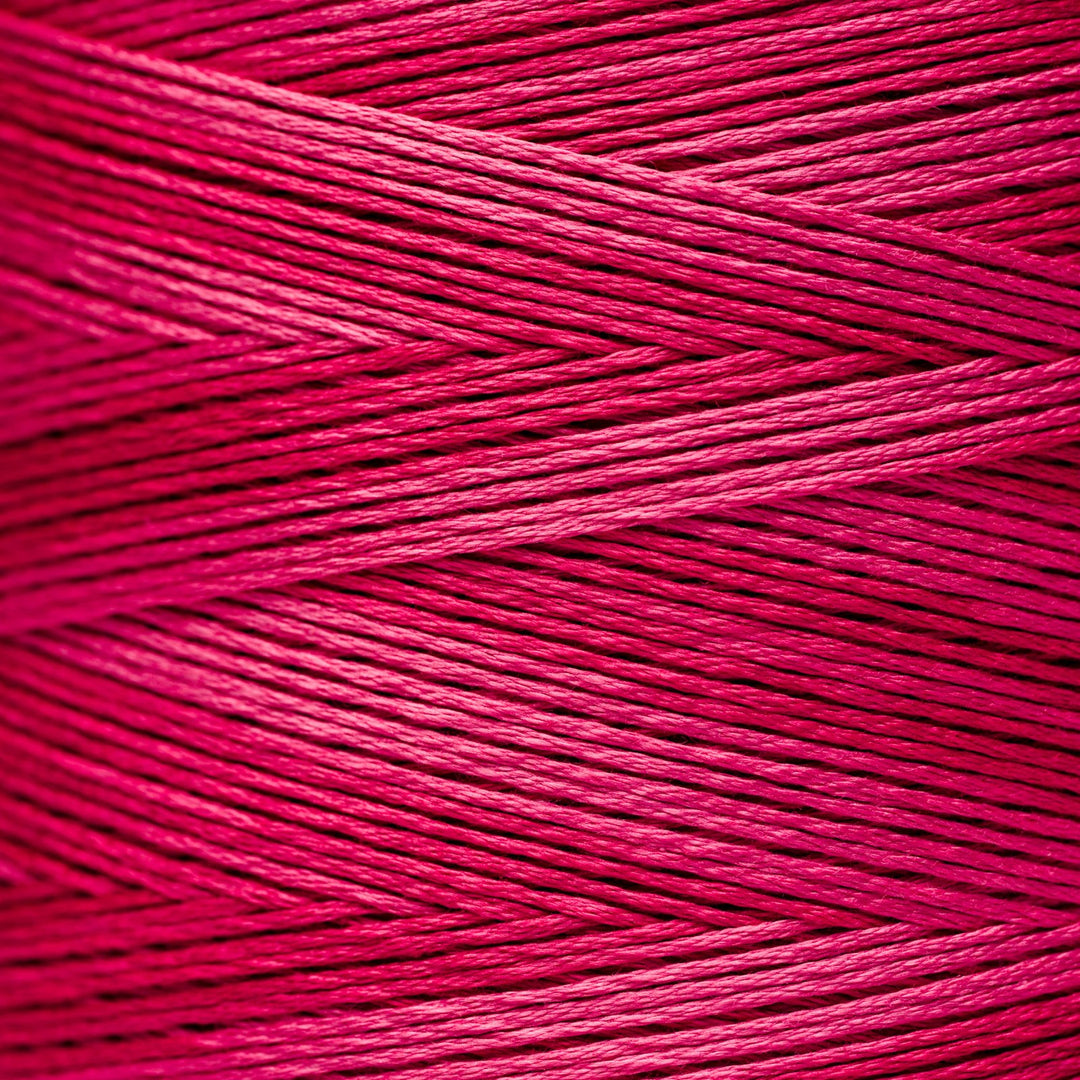 A close-up of bright pink floss thread wound in parallel strands, filling the entire frame.
