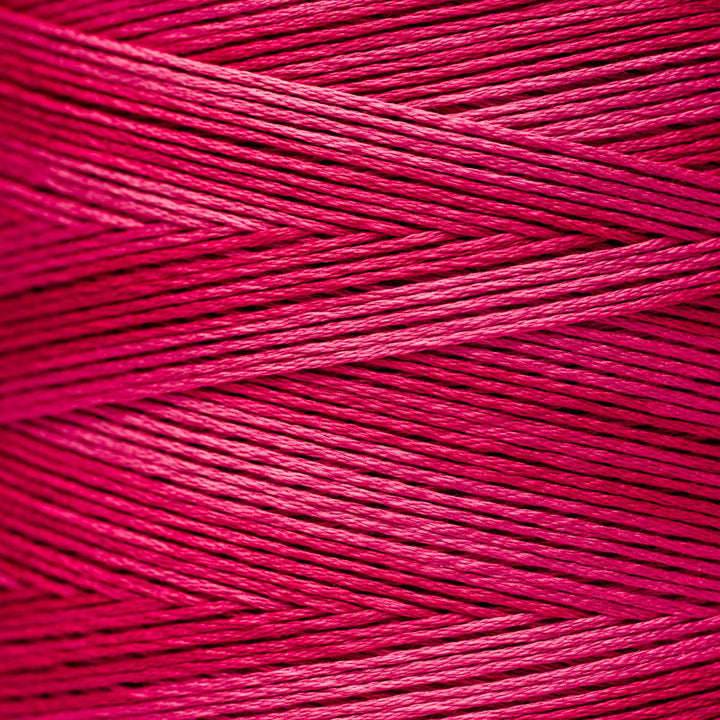 A close-up of bright pink floss thread wound in parallel strands, filling the entire frame.