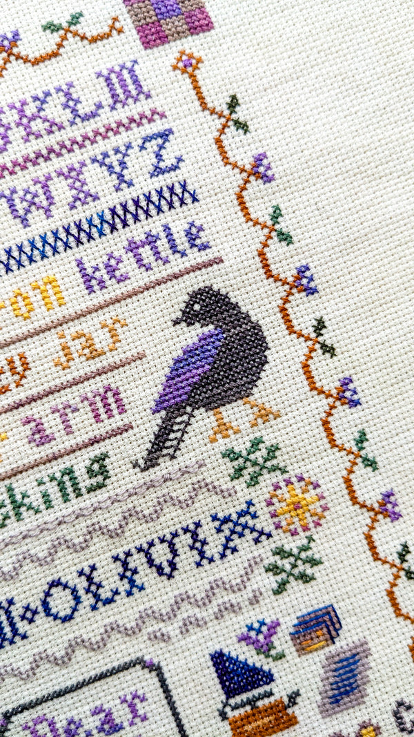 Cross-stitched design with a bird, text, and decorative elements on fabric.