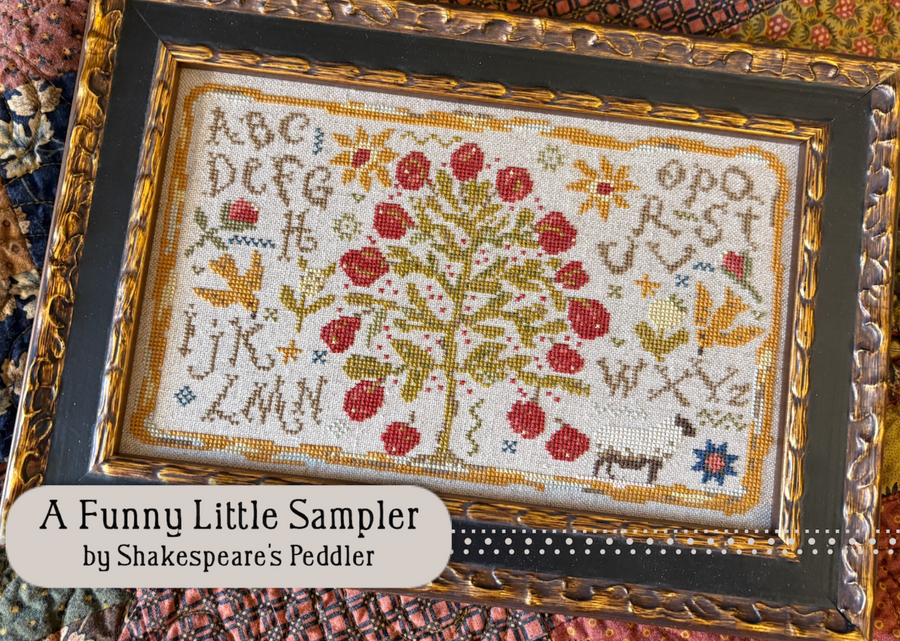 Cross-stitched sampler with alphabet and floral design, framed in gold and black.