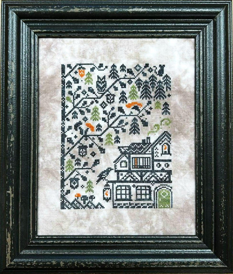 Framed cross-stitched pattern of a house and trees on a textured fabric background