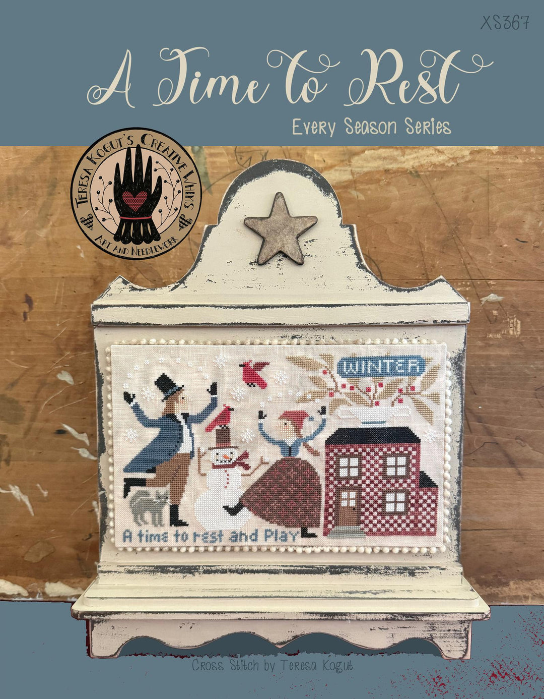 Cross-stitched design of a winter scene with people and a snowman, on a wooden background with a brand logo.