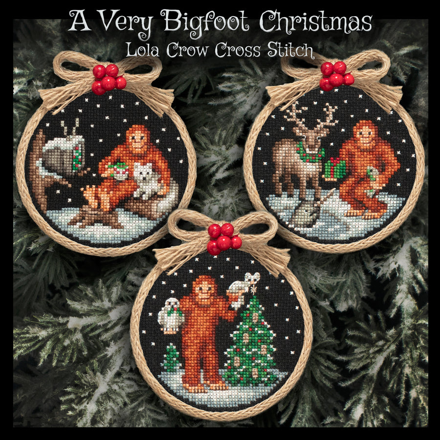 Three circular cross-stitch ornaments displayed on a dark green pine background, with the text 'A Very Bigfoot Christmas' and 'Lola Crow Cross Stitch' at the top. Each ornament features a different Bigfoot holiday scene: one with a campfire and animal, one with a deer, and one standing by a Christmas tree.