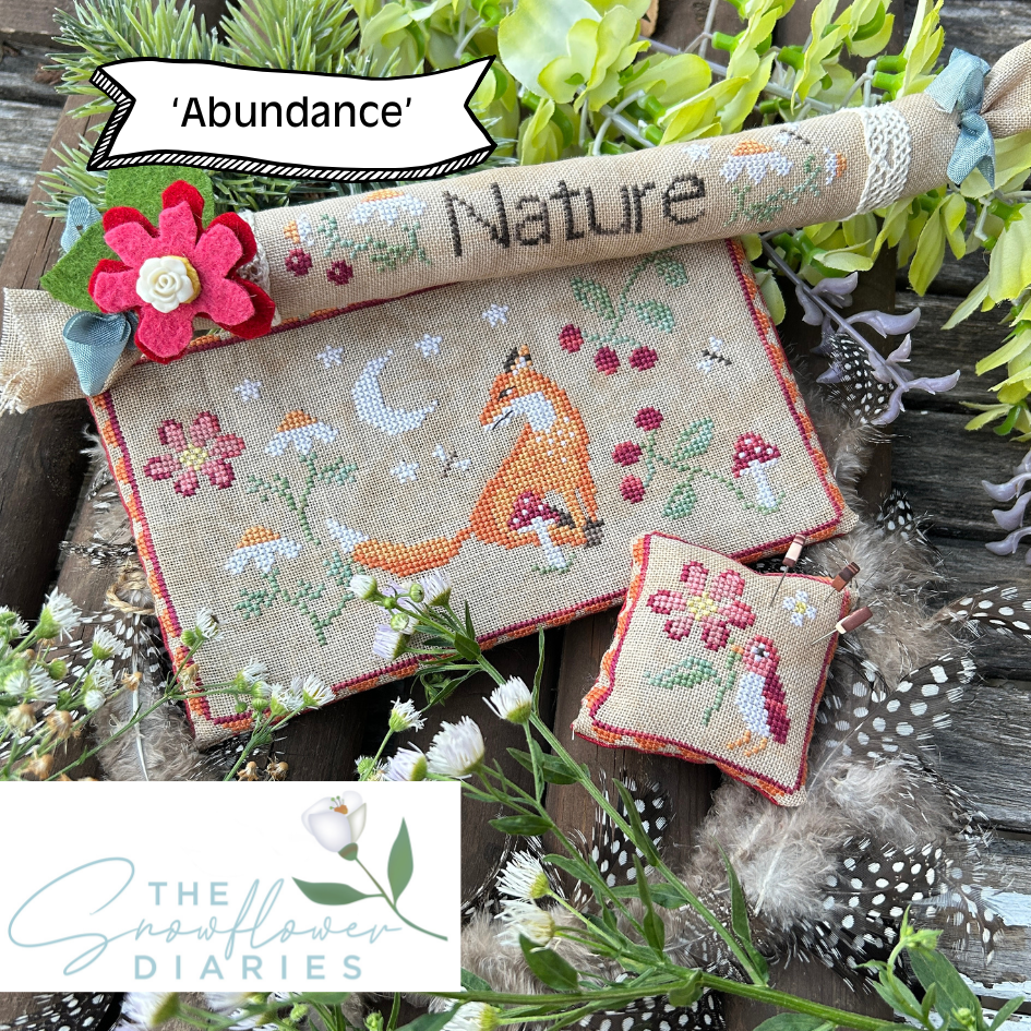 Cross-stitched nature-themed items with foxes and flowers on a wooden surface with greenery.