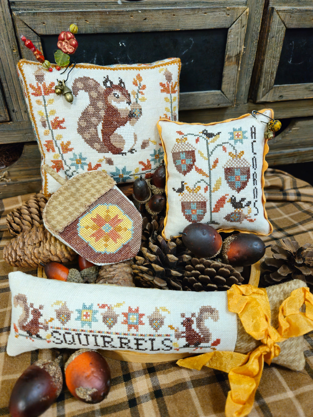 Decorative pillows with cross-stitched designs featuring squirrels and autumn elements on a rustic background.