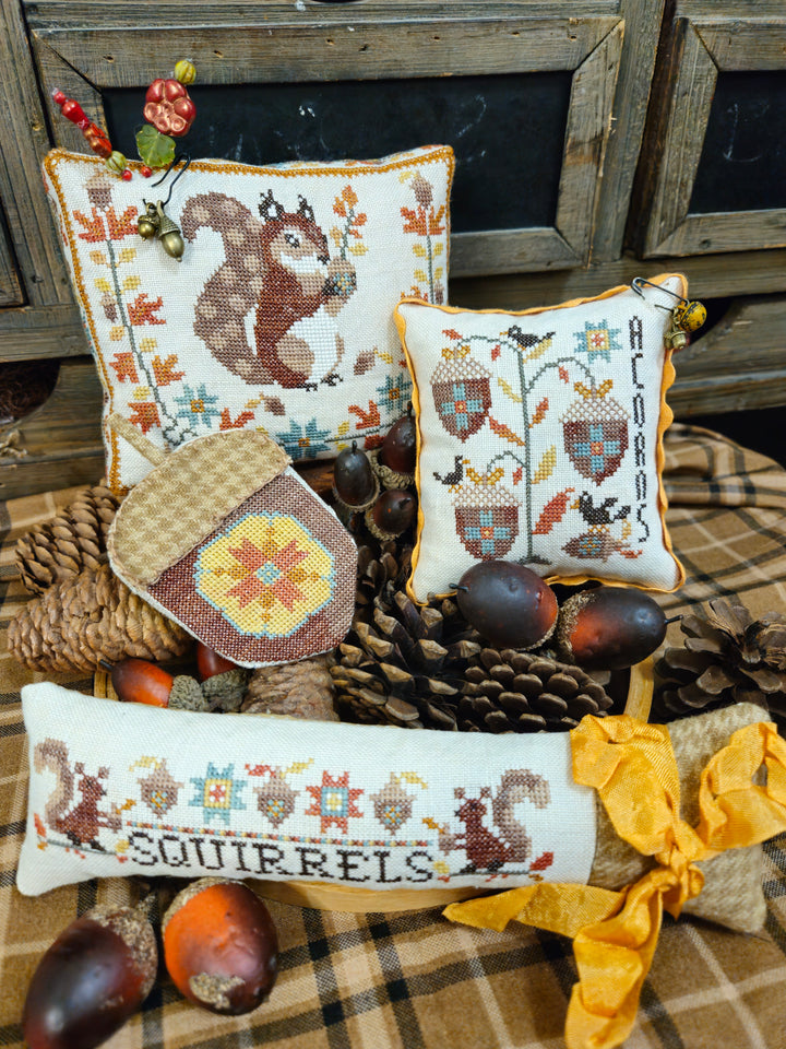 Decorative pillows with cross-stitched designs featuring squirrels and autumn elements on a rustic background.