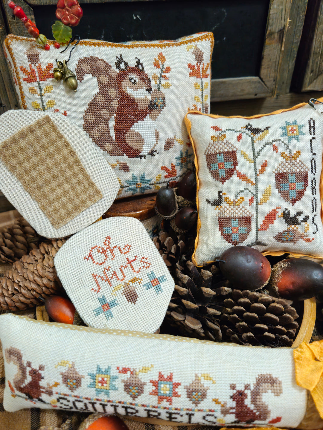 Collection of cross-stitched pillows with autumn-themed designs on a wooden surface.