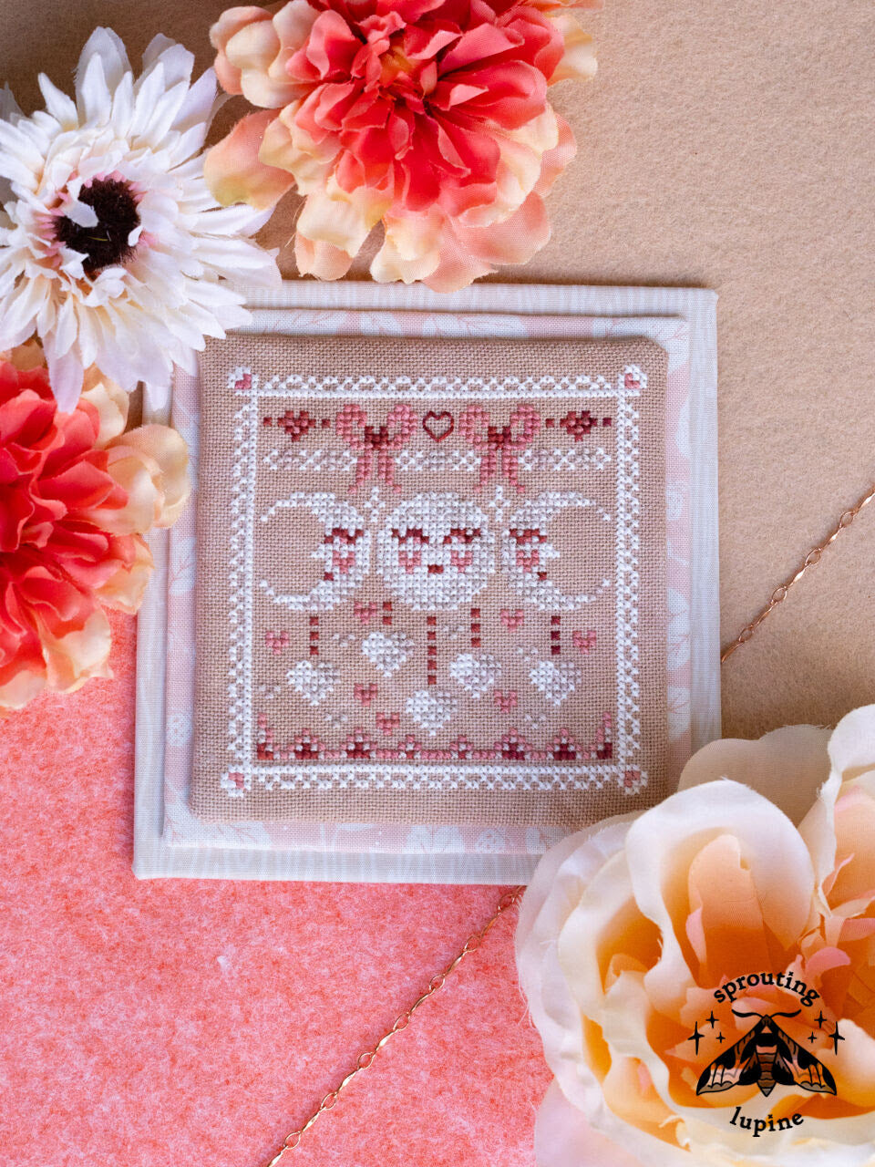 a small valentine design featuring three moon phases, hearts and bows in white and pink thread 