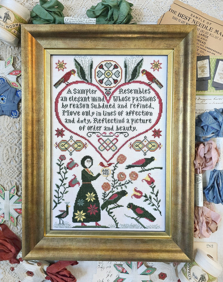 Framed cross-stitched sampler with decorative elements on a textured background