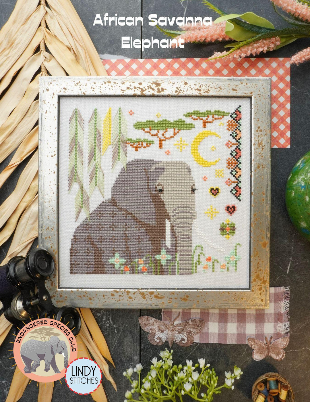 Cross-stitched pattern of an elephant in a frame with decorative elements on a textured surface.