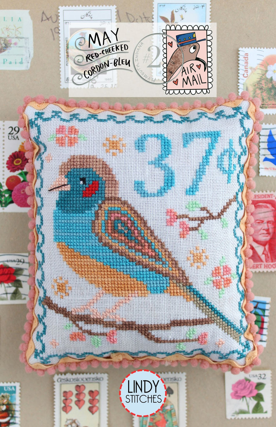 Cross-stitched pillow with a bird design and postal-themed decorations, featuring the Lindy Stitches brand.