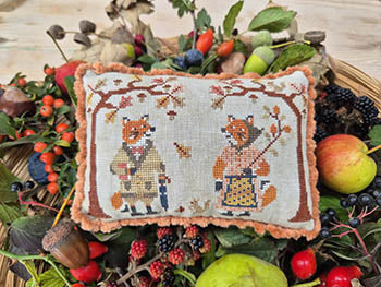 Decorative pillow with fox design surrounded by fruits and leaves on a wooden surface
