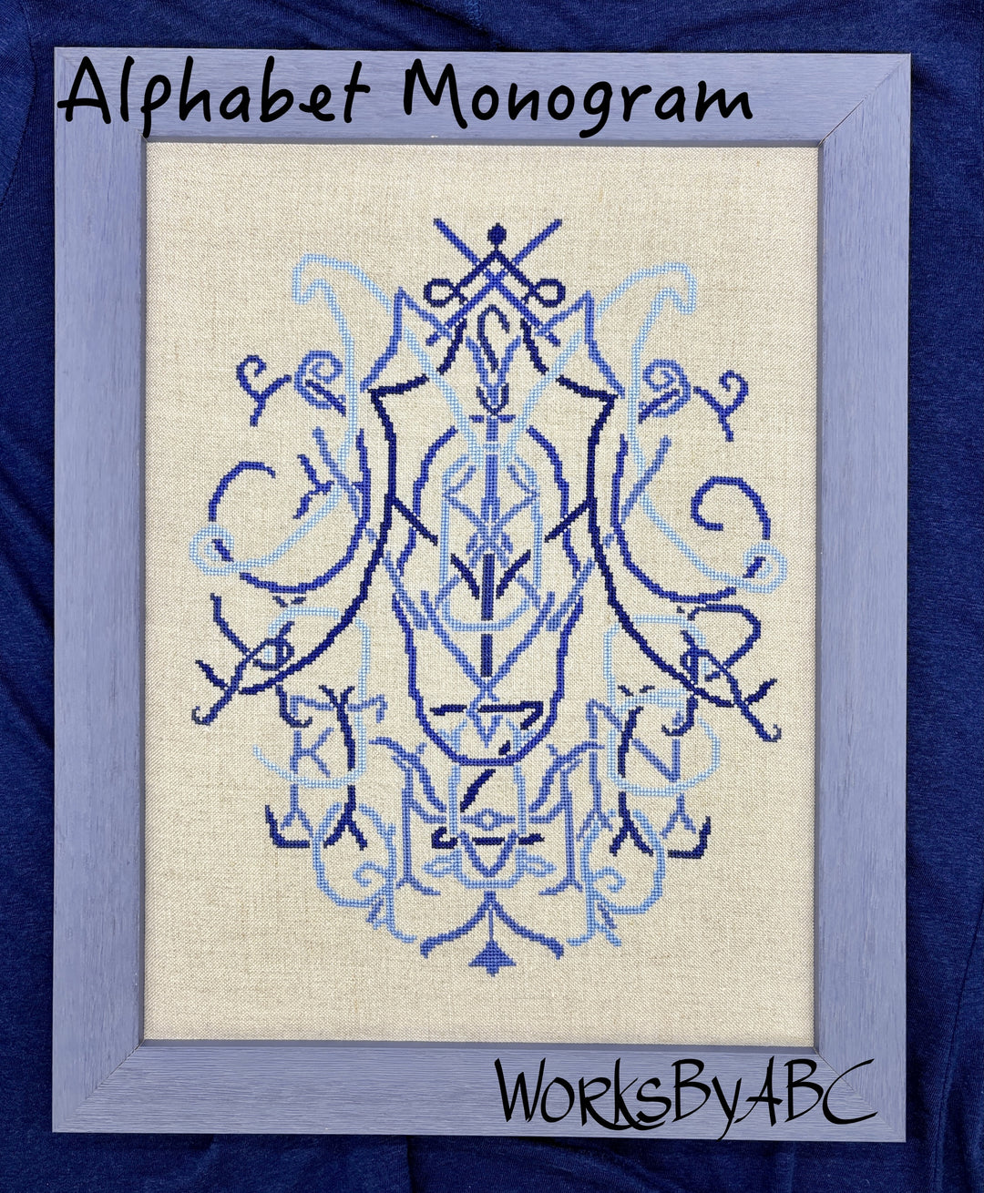 A framed alphabet monogram needlepoint or embroidery design featuring a symmetrical crest in shades of blue on a cream fabric background, enclosed in a light blue frame against a dark blue backdrop. Text overlays read 'Alphabet Monogram' and 'WorksBy4BC'.