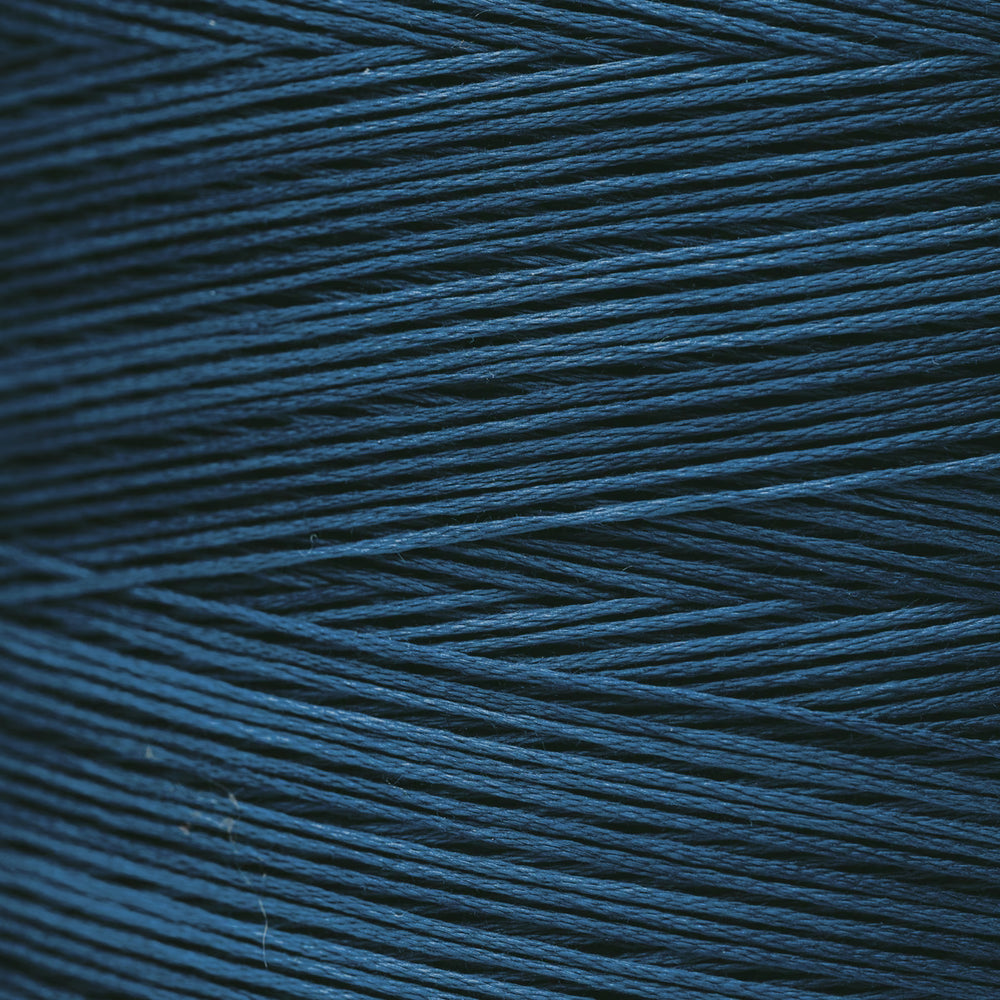 A close-up texture shot of dark teal blue thread strands wound together, showing the fine thread details and color.