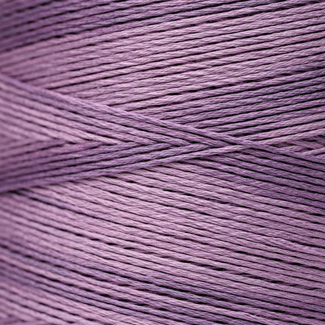 A close-up of lavender purple thread wound into a cone, showing the detailed texture of the twisted thread.