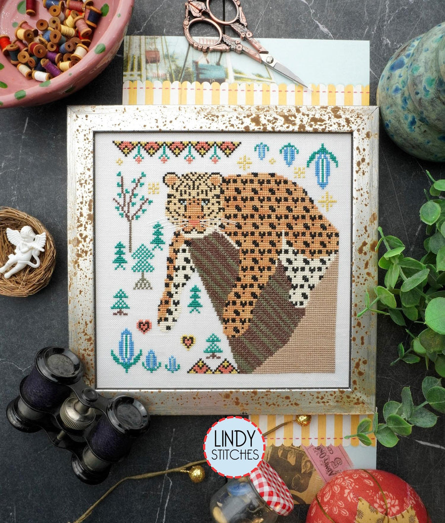 a cross-stitch kit depicting an Amur leopard displayed alongside crafting tools like scissors and a spool of thread,