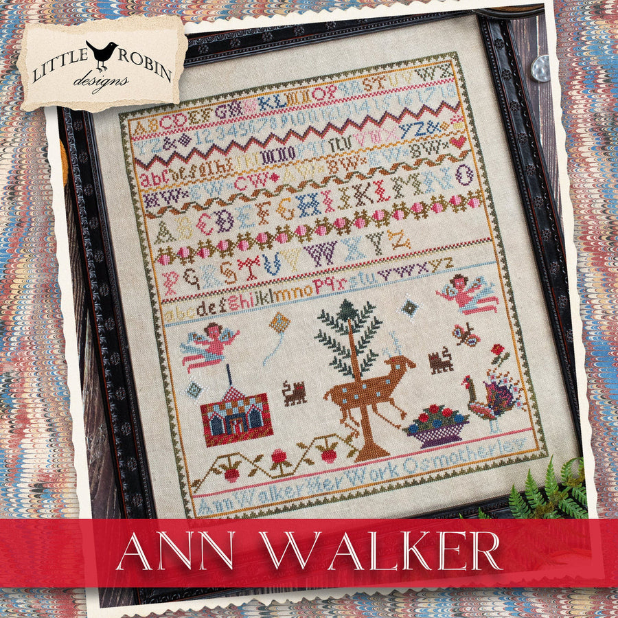 A framed cross-stitch sampler featuring the 'Ann Walker' alphabet and folk motifs, presented on a patterned textile background with a 'Little Robin Designs' label and 'Ann Walker' banner.