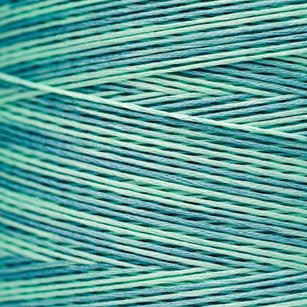 A close-up texture shot of variegated thread wound in a herringbone pattern, showing alternating shades of teal, mint green, and light aqua.