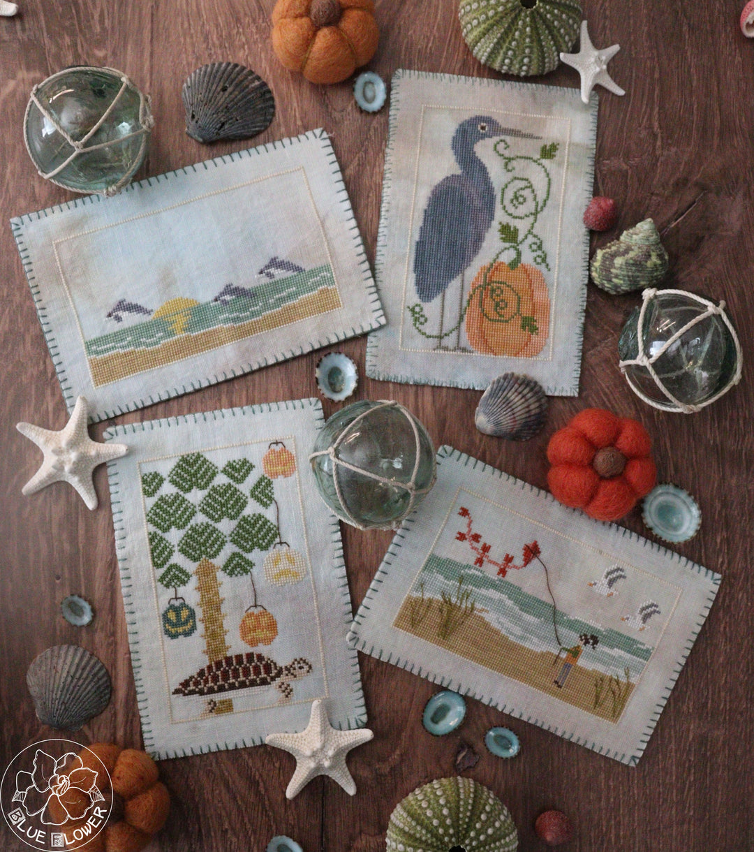 set of four postcard style stitches featuring beach scenes with autumn elements like pumpkins and fall colors 