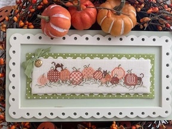 Cross-stitched design of pumpkins and leaves on a white background with decorative frame.