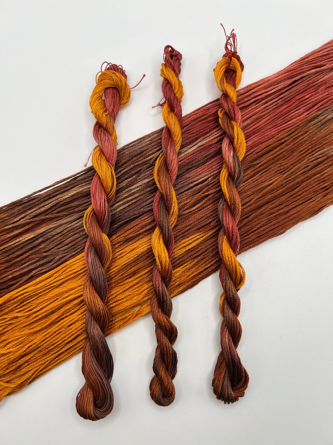 Three braided strands of yarn in brown, orange, and red on a white background