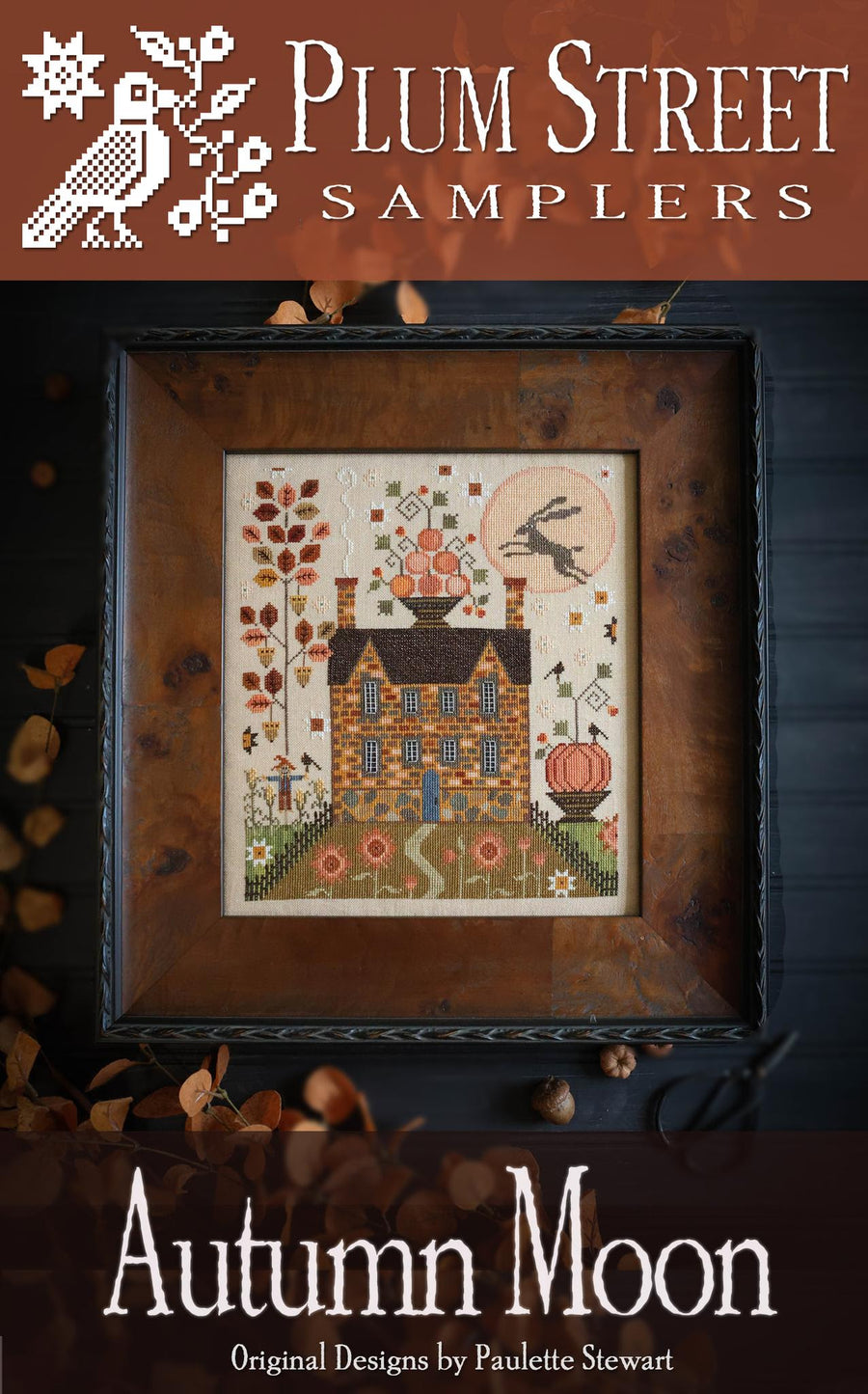 Framed cross-stitch pattern titled 'Autumn Moon' by Plum Street Samplers on a dark background.