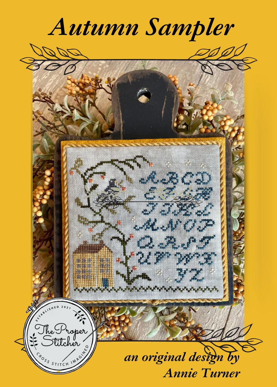 Cross-stitched sampler with alphabet and bird design on a yellow background, featuring 'The Proper Stitcher' logo.