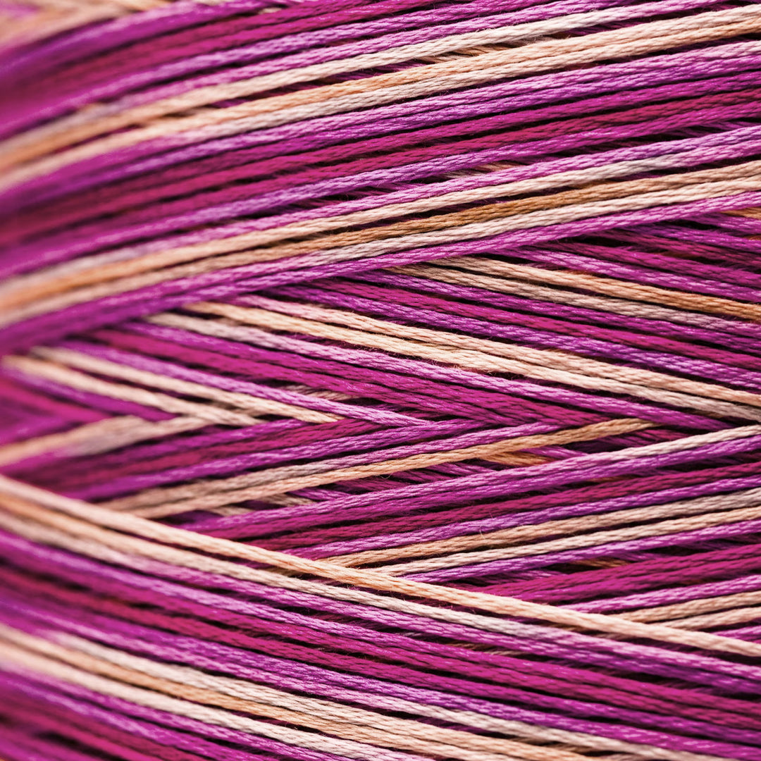 Close-up of variegated embroidery thread wound in a cone, showing alternating stripes of magenta pink, deep purple, and light peach-beige.