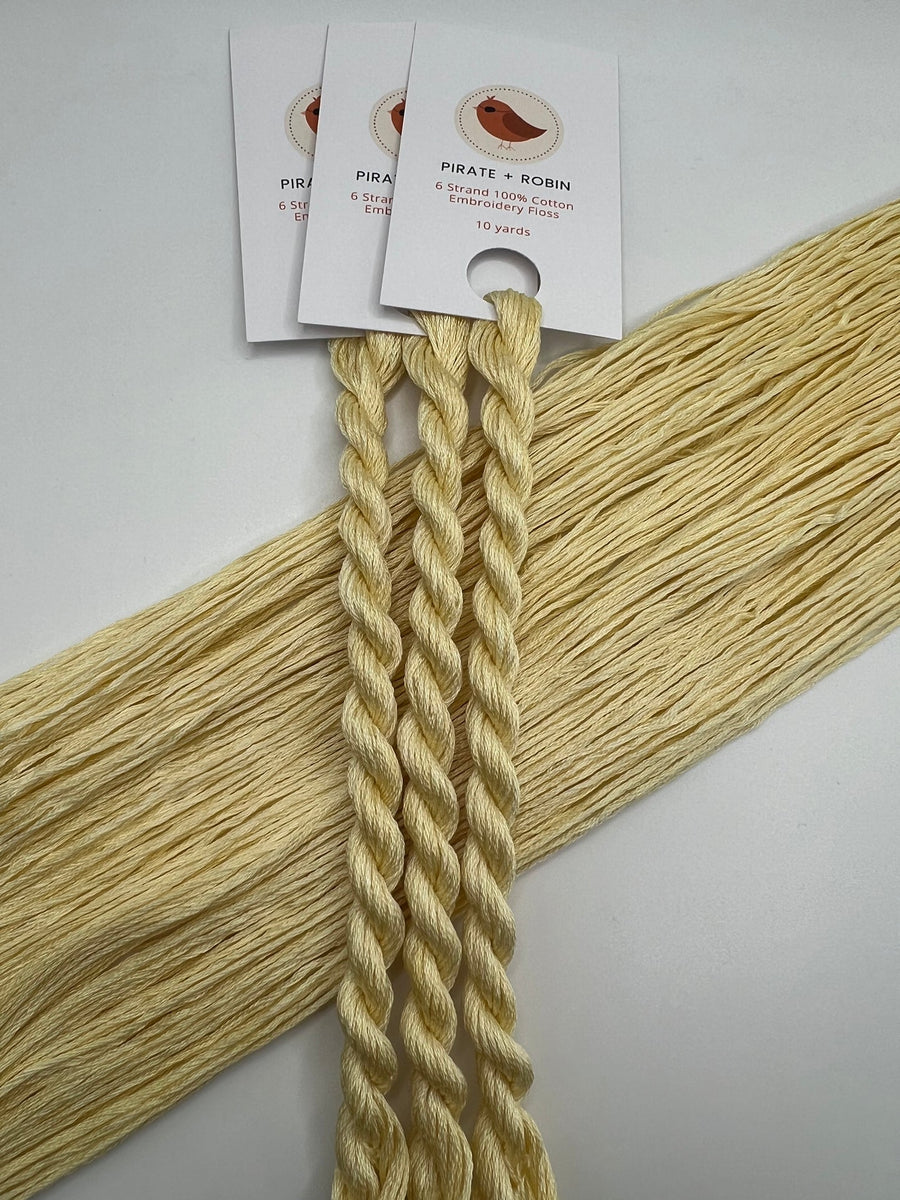 three braided light yellow floss skeins with tags on a light gray background