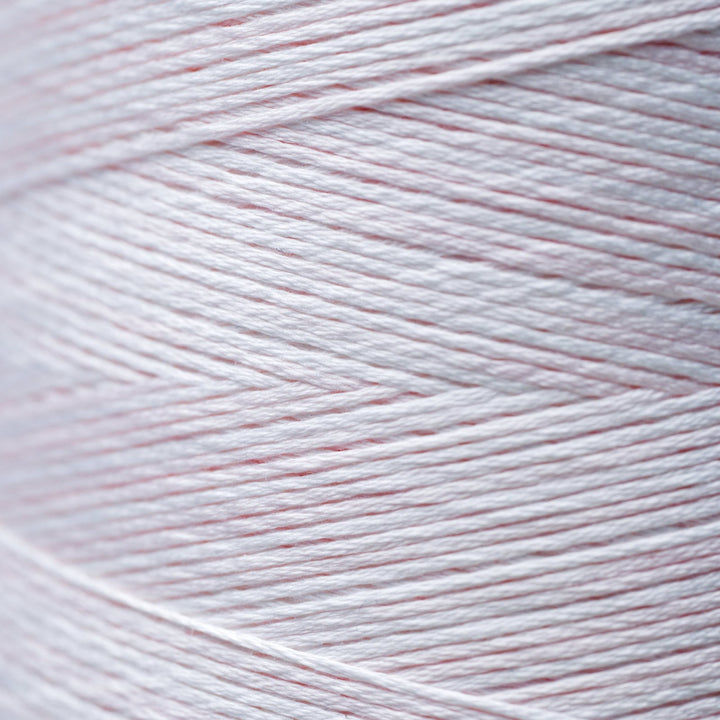 A close-up of light pink and white yarn wound on a cone, showing the fine texture of the thread.