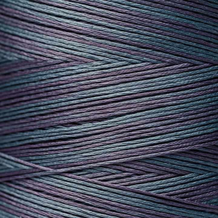 A close-up of variegated yarn with a repeating chevron pattern in dark teal blue and muted plum purple.