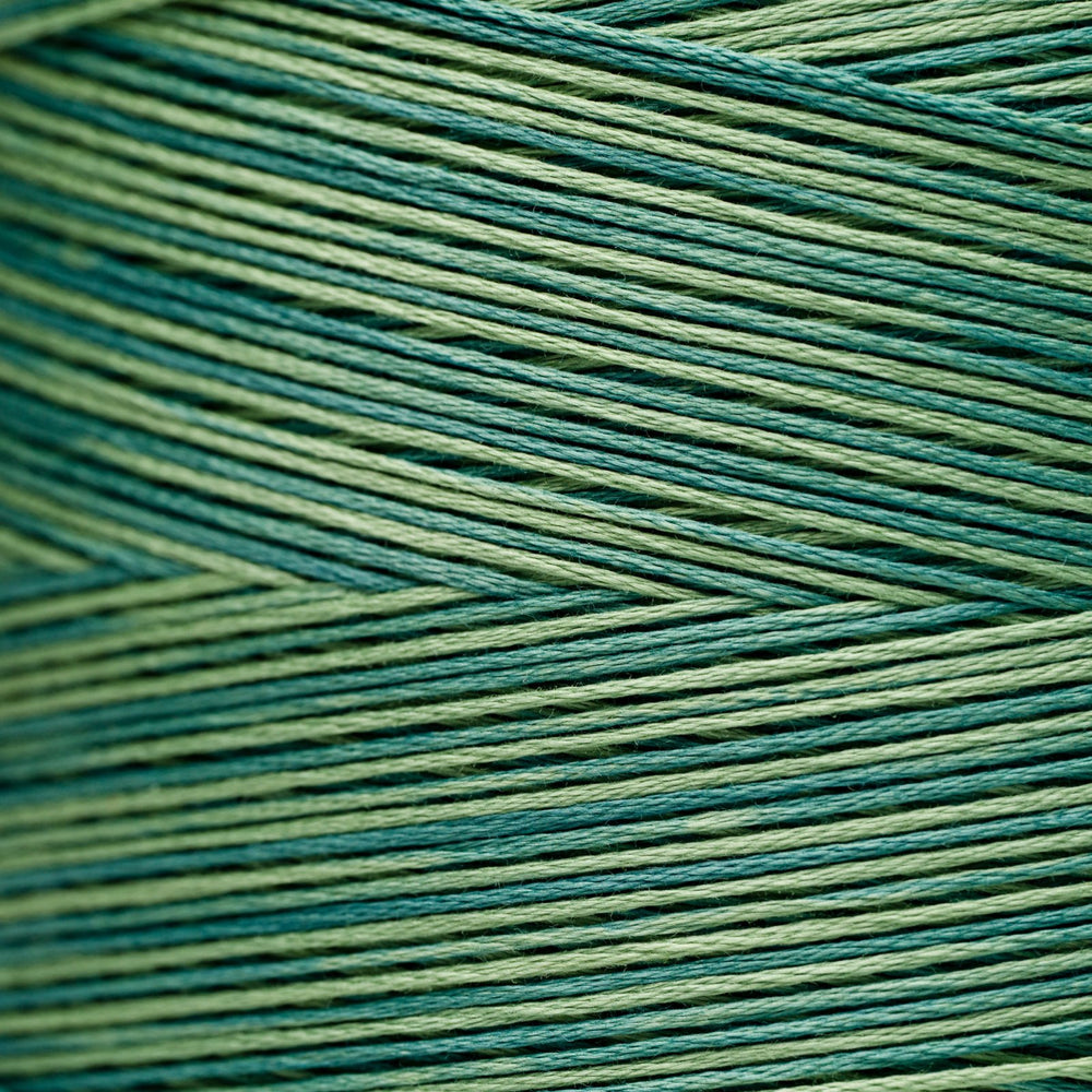 A close-up of tightly wound thread strands in alternating shades of teal blue and light olive green, arranged in a textured chevron pattern.