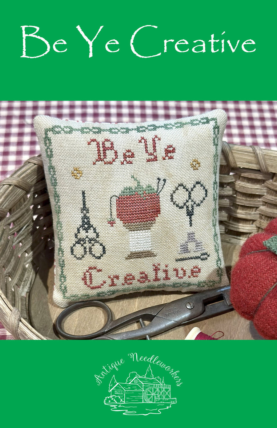 Decorative pillow with cross-stitch design and text 'Be Ye Creative' in a basket with sewing tools.