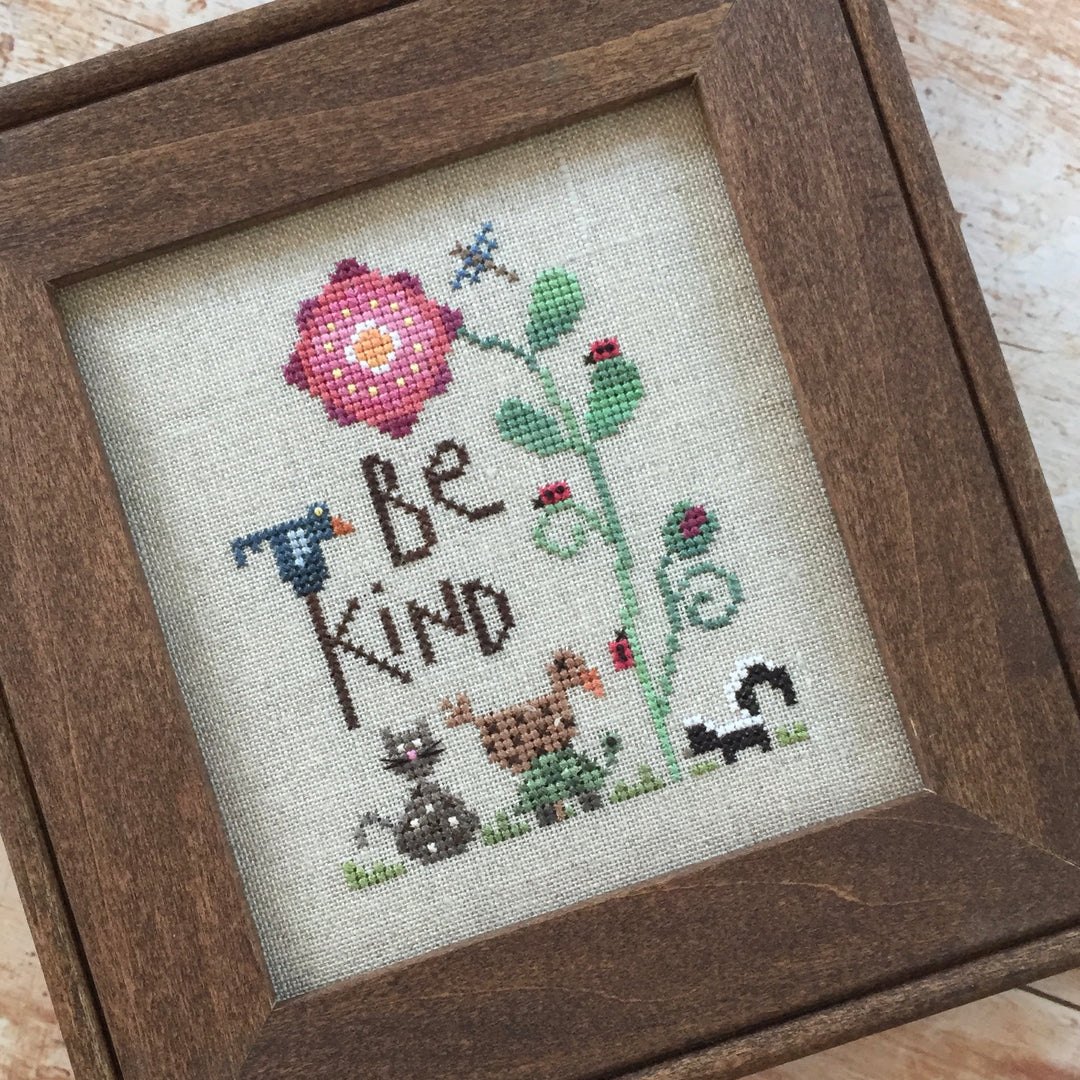 Cross-stitched picture with 'Be Kind' text and animals in a wooden frame.