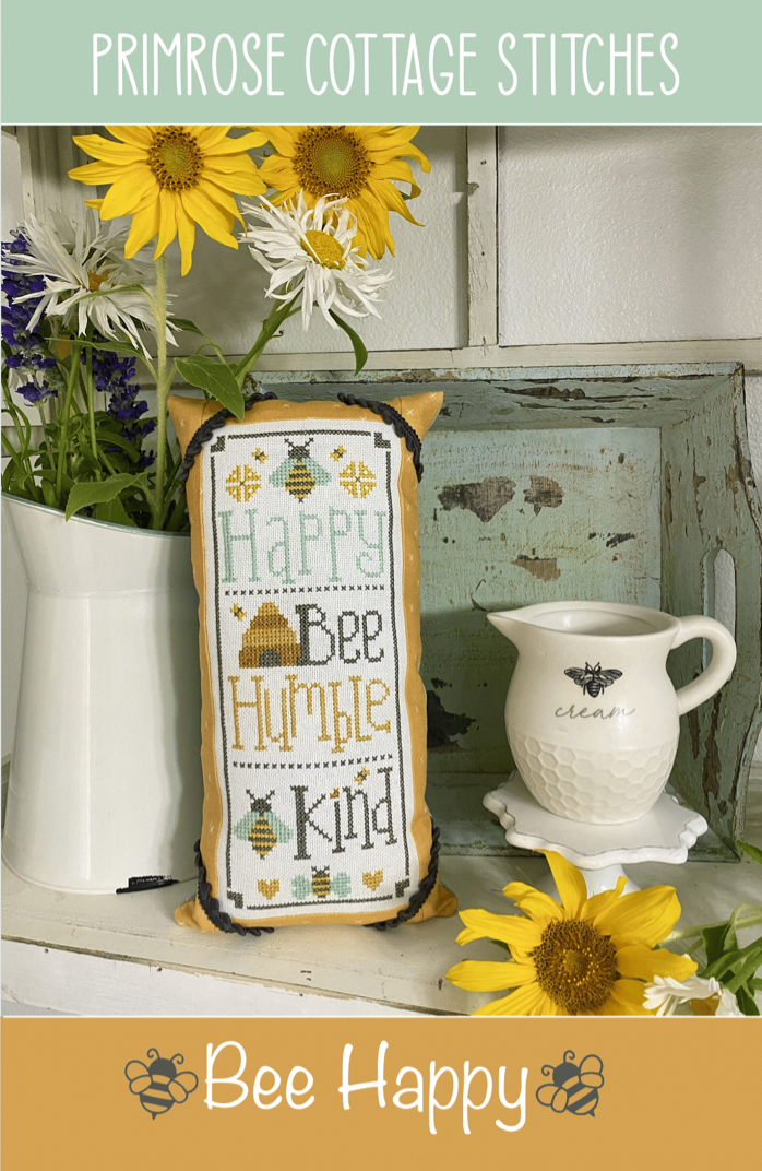 Decorative pillow with 'Happy Bee Humble Kind' text on a shelf with flowers and a teacup.
