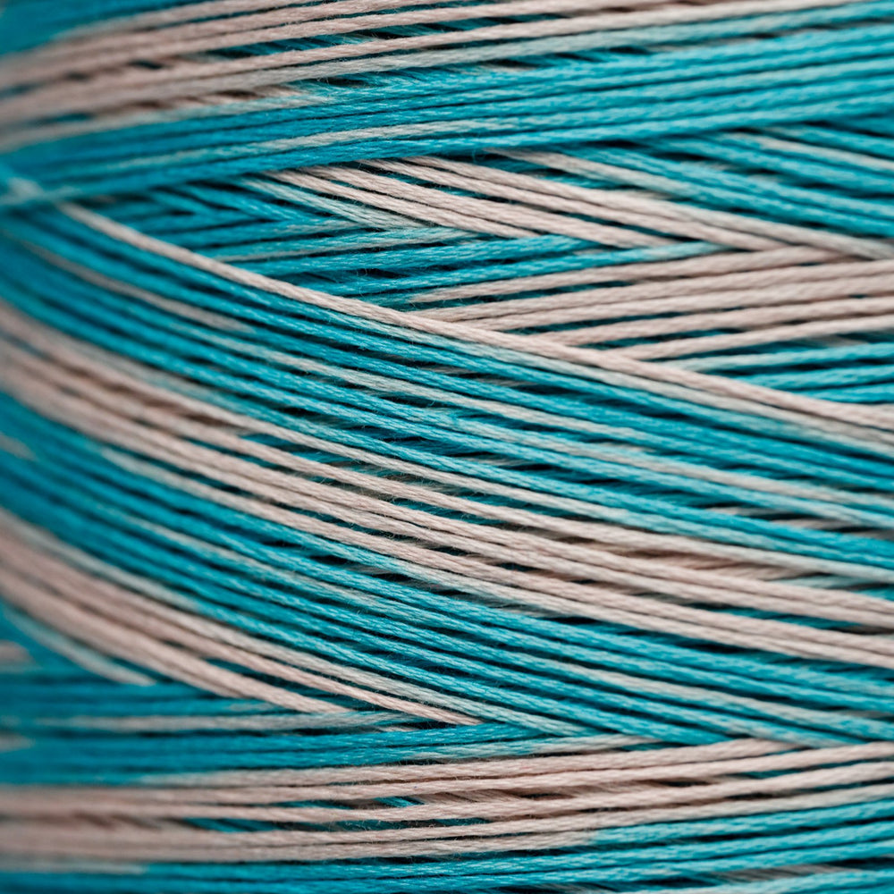 Close-up of wound thread spool in alternating turquoise blue and light beige colors, showing the texture and color pattern of the thread.