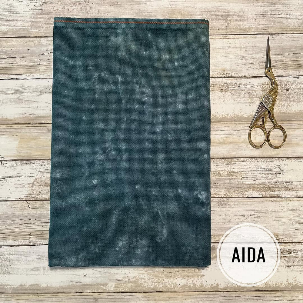 Teal fabric with a textured pattern on a wooden surface with scissors and 'AIDA' branding.