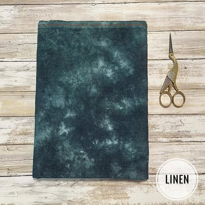 Dark green linen fabric on a wooden surface with a pair of scissors.