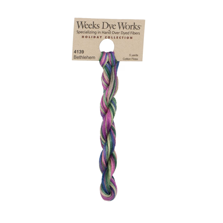 A single twisted skein of Weeks Dye Works Bethlehem cotton thread from the Holiday Collection, featuring a multicolor blend of purple, green, blue, and pink, attached to a kraft paper hanger.