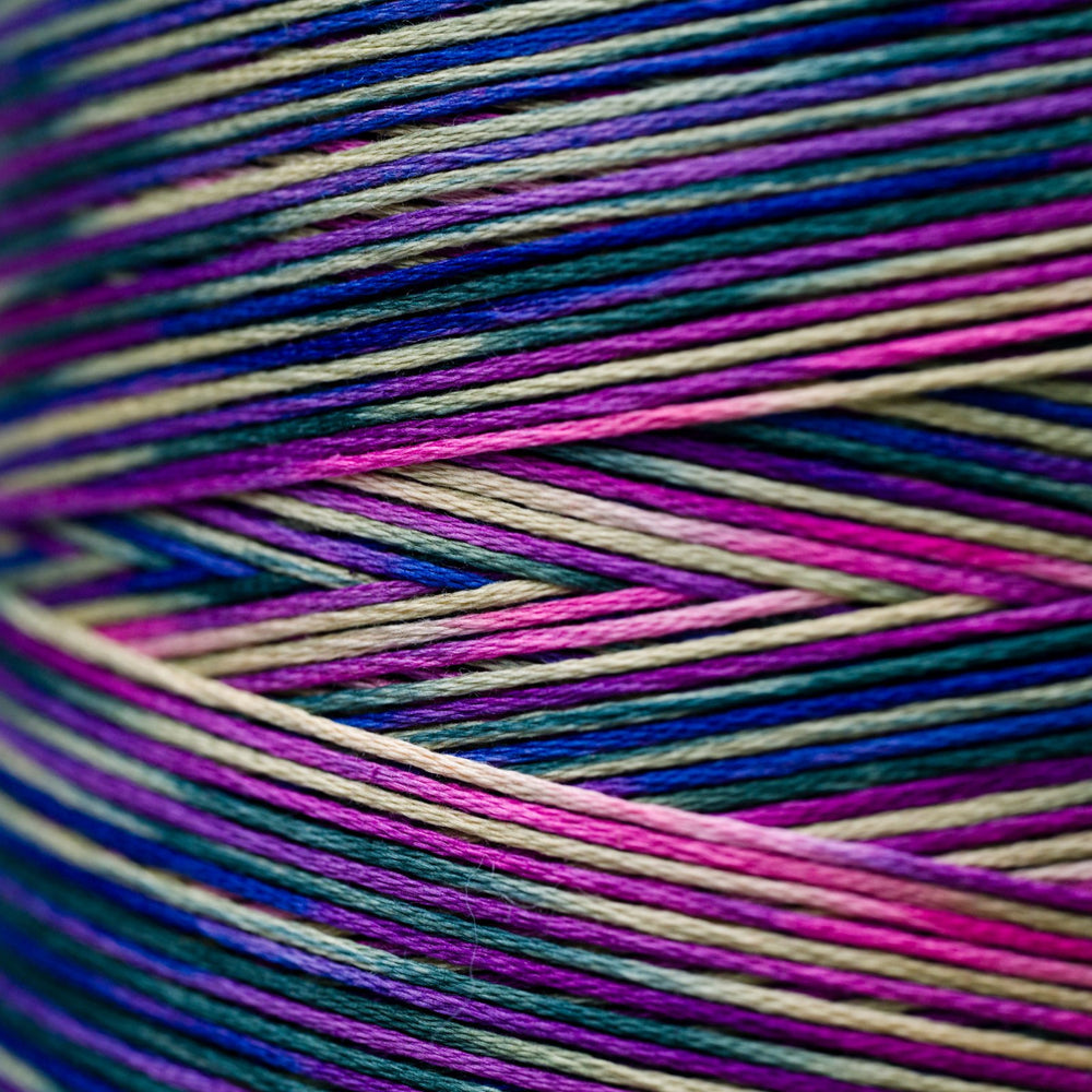 Close-up of a skein of variegated thread with alternating stripes of magenta pink, deep blue, purple, and cream.