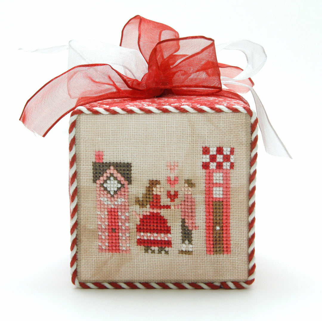 Decorative box with cross-stitched design and red ribbon on a white background