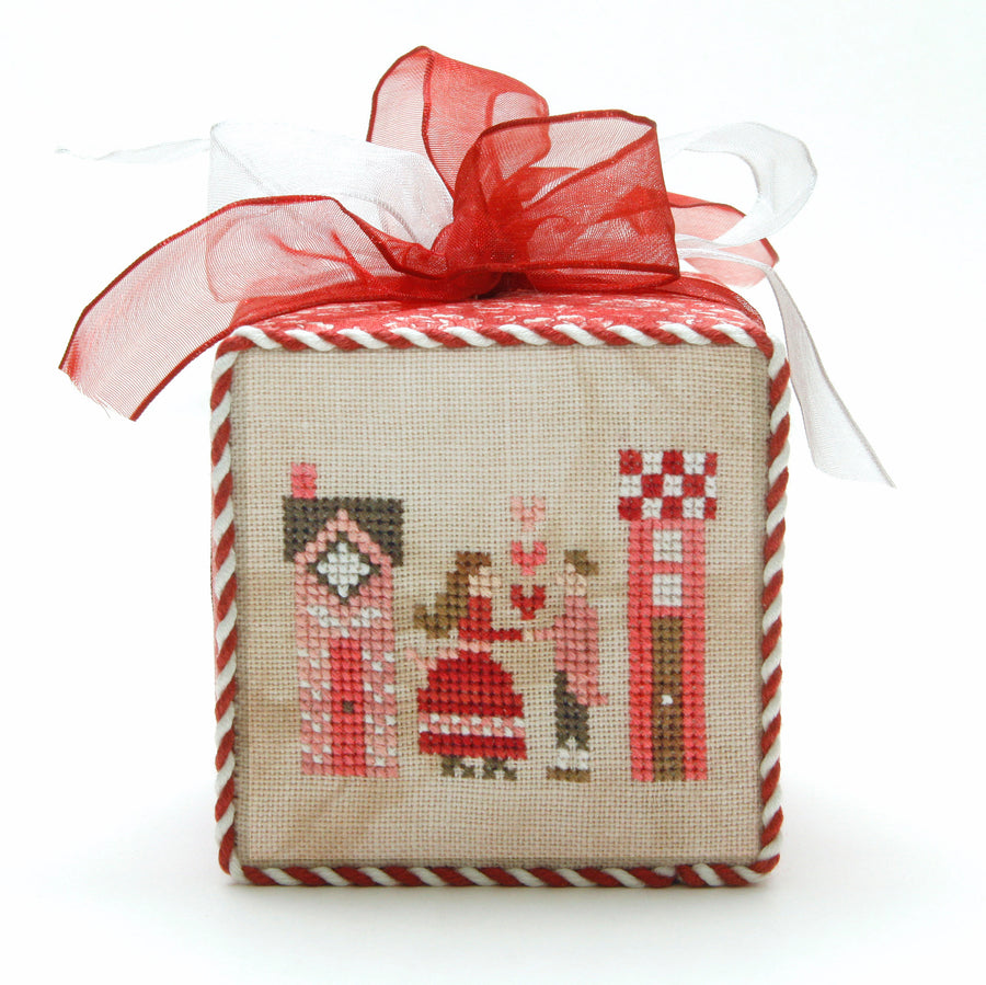 Decorative box with cross-stitched design and red ribbon on a white background