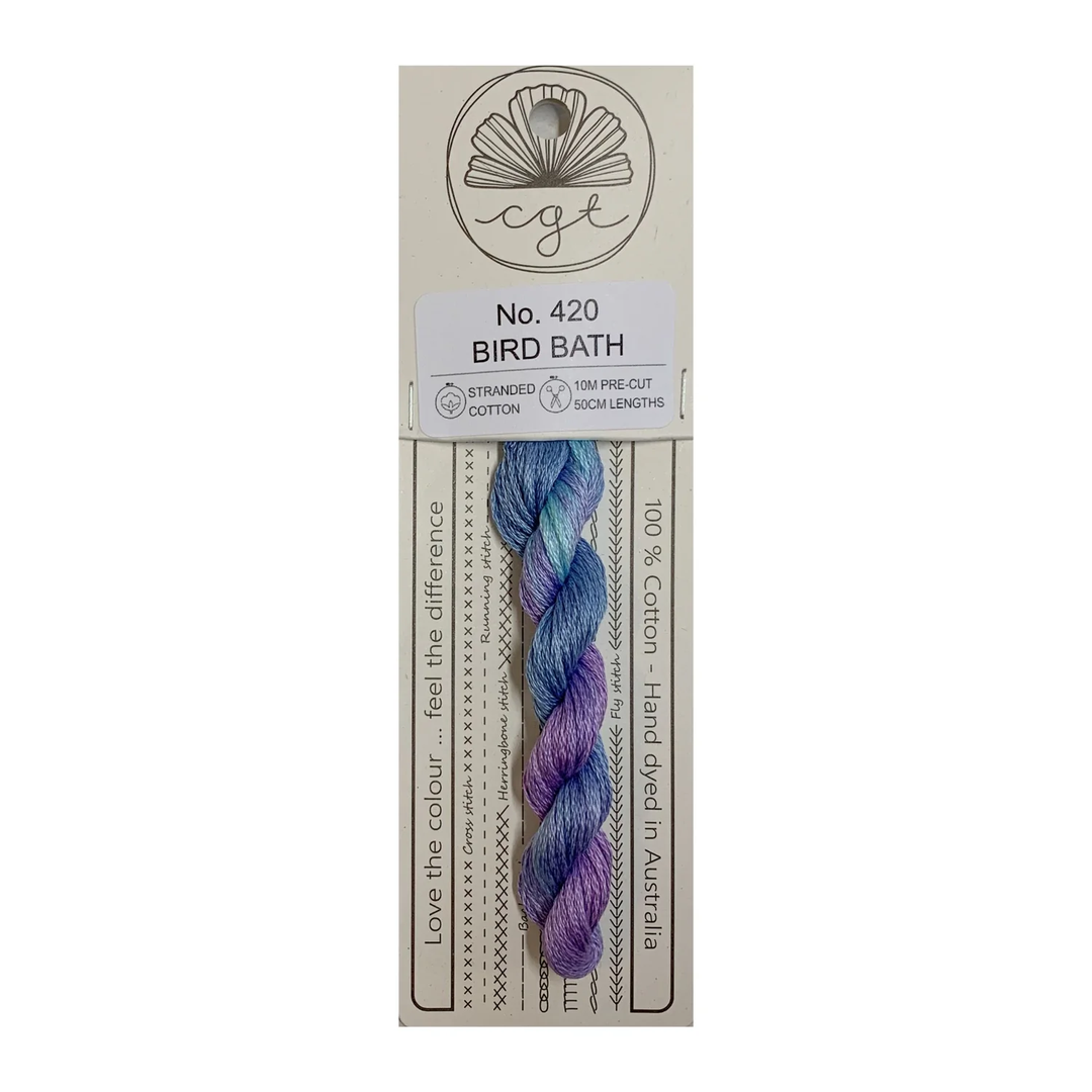 Packaged yarn with a purple and blue skein on a beige label with text and branding.
