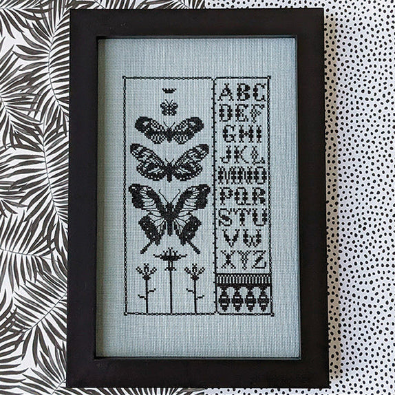 Black butterfly sampler cross stitch pattern with alphabet letters on a white background