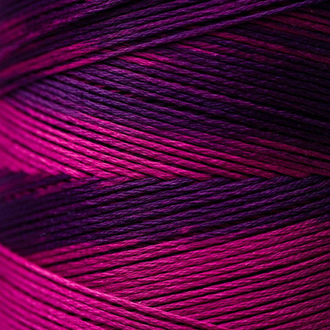 A close-up of variegated thread strands showing a color-shifting gradient from bright magenta pink to deep purple and black.