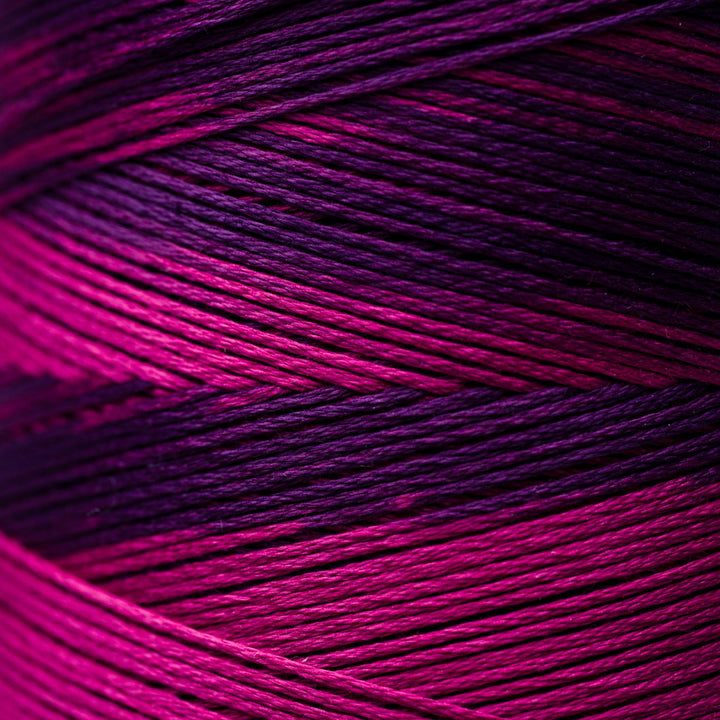 A close-up of variegated thread strands showing a color-shifting gradient from bright magenta pink to deep purple and black.