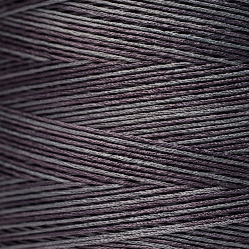 A close-up texture shot of multi-ply thread wound in a cone, showing fine strands twisted into dark purple and gray threads.
